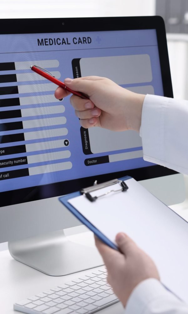 Doctor using computer to fill out patient's medical card at table in clinic, closeup